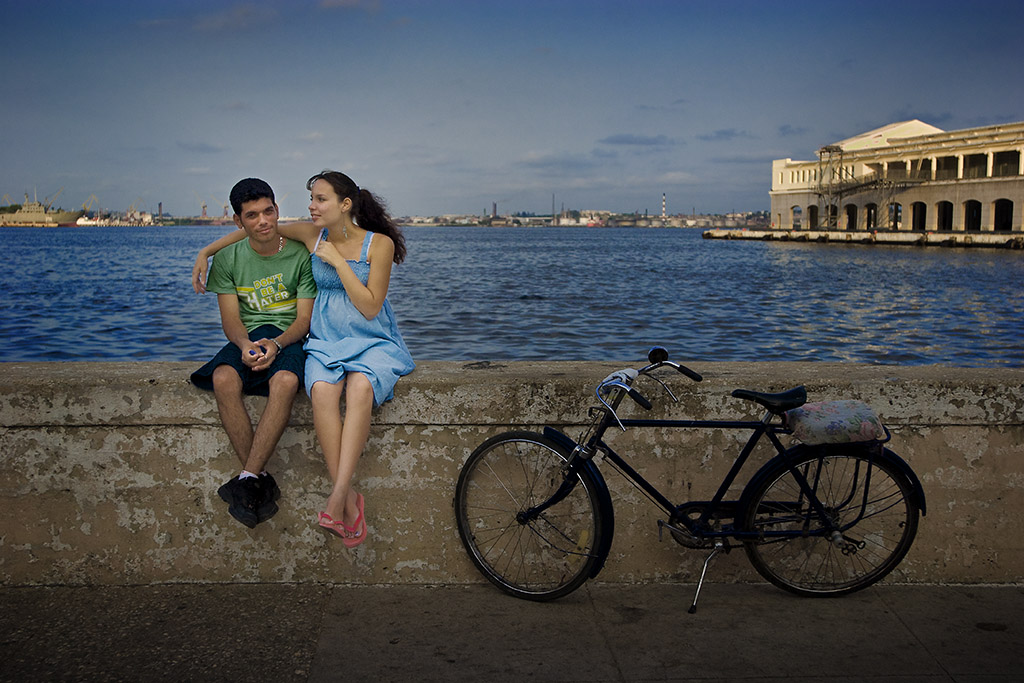 a couple sitting on a wall near the Havana Harbor